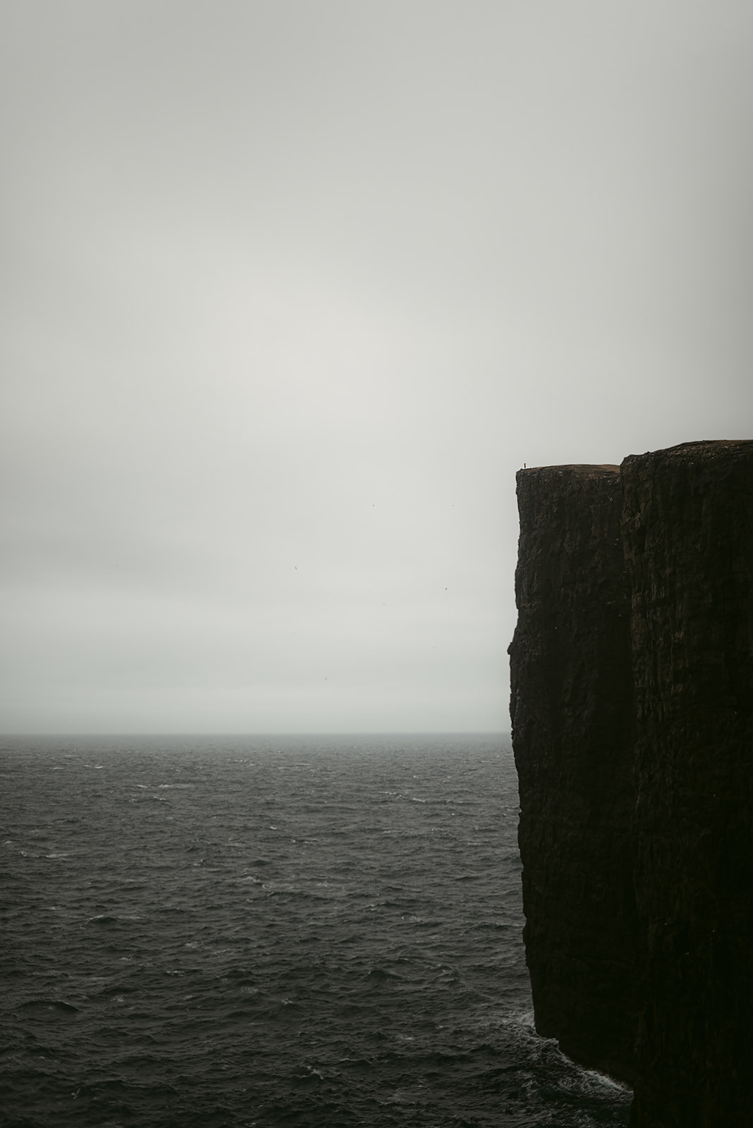 Steep vertical cliff against dark, cloudy sky