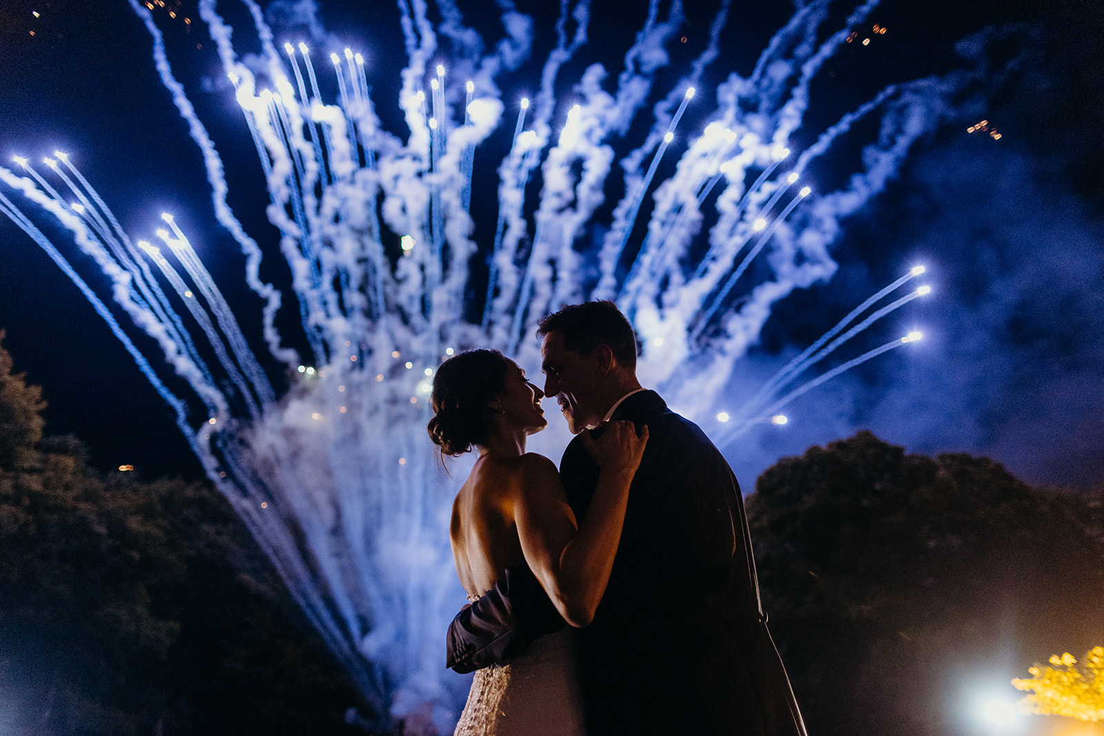bride and groom looking at each other as bright blue fireworks explode in background