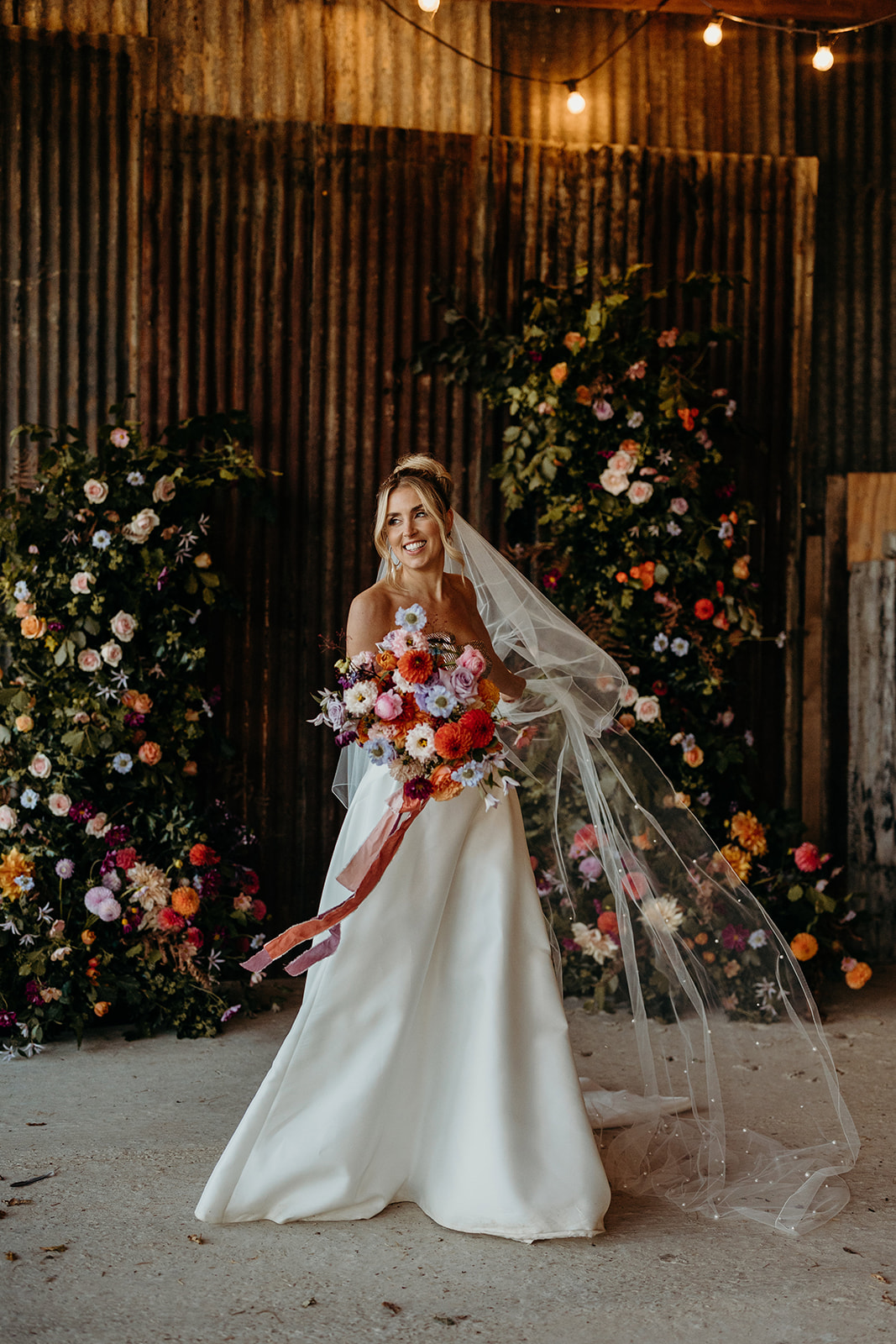 bride holding colouful bouquet smiling as veil blows to one side
