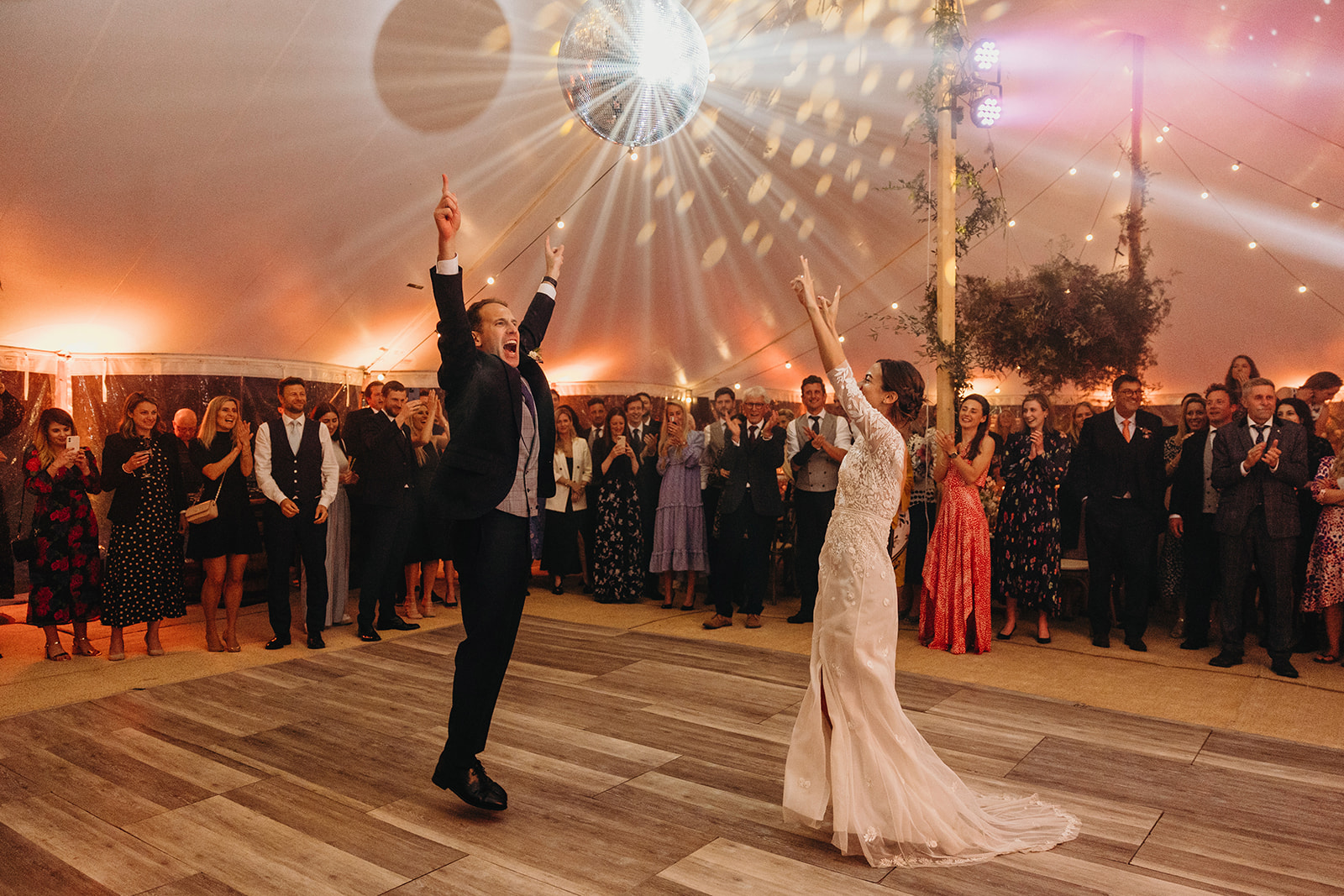Couple first dance with hands in air as disco ball illuminates dancefloor