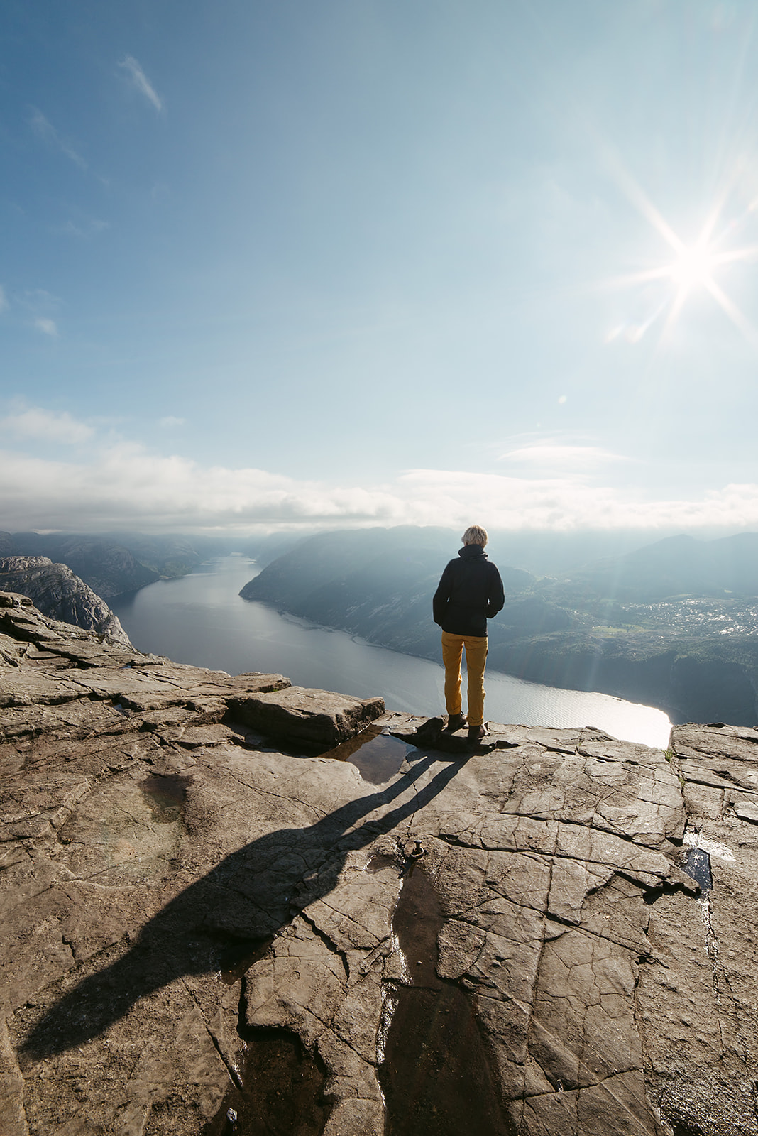 Person standing at cliff overlooking a fjord