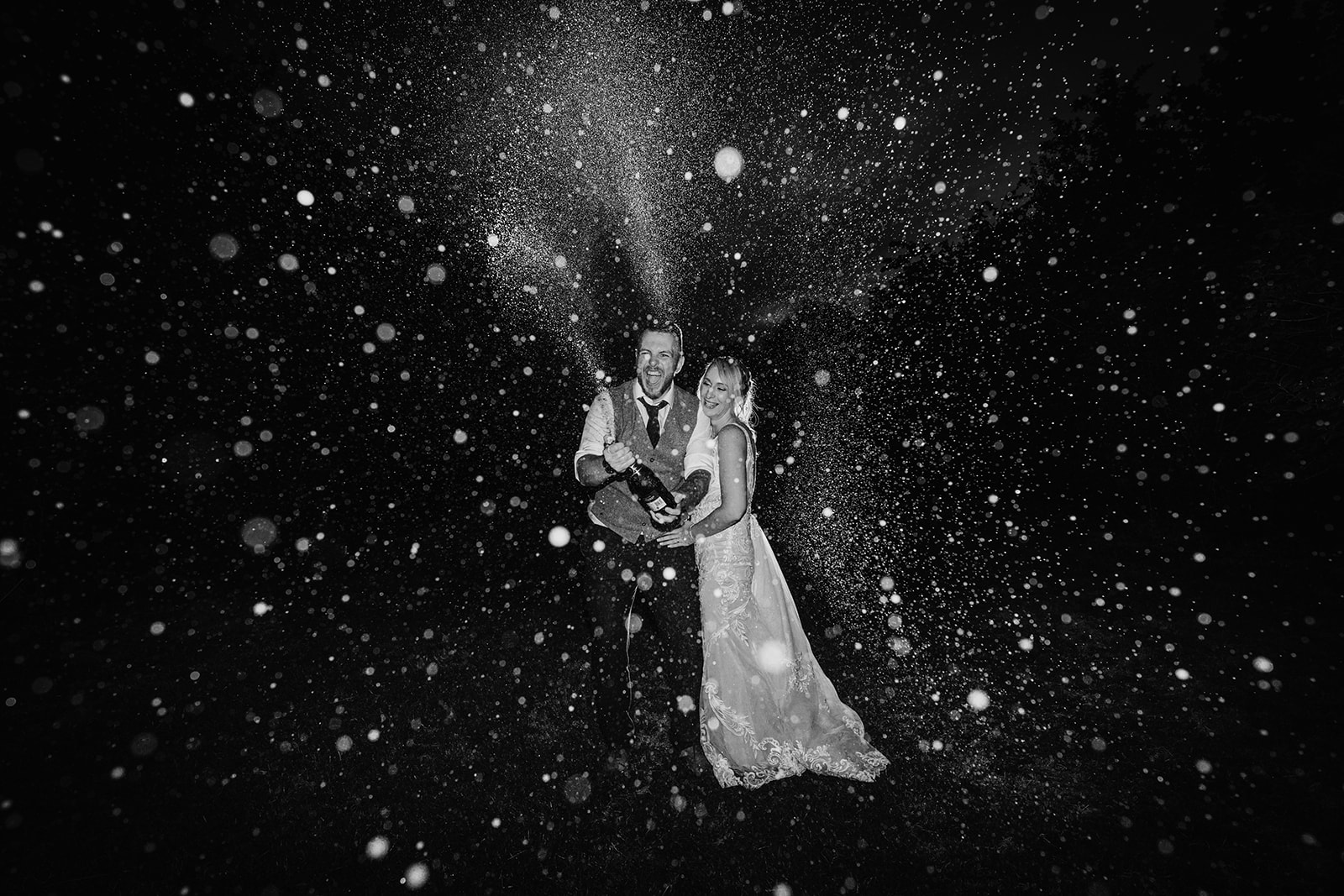 a black and white picture of the bride and groom spraying champagne at night by a Bristol wedding photographer