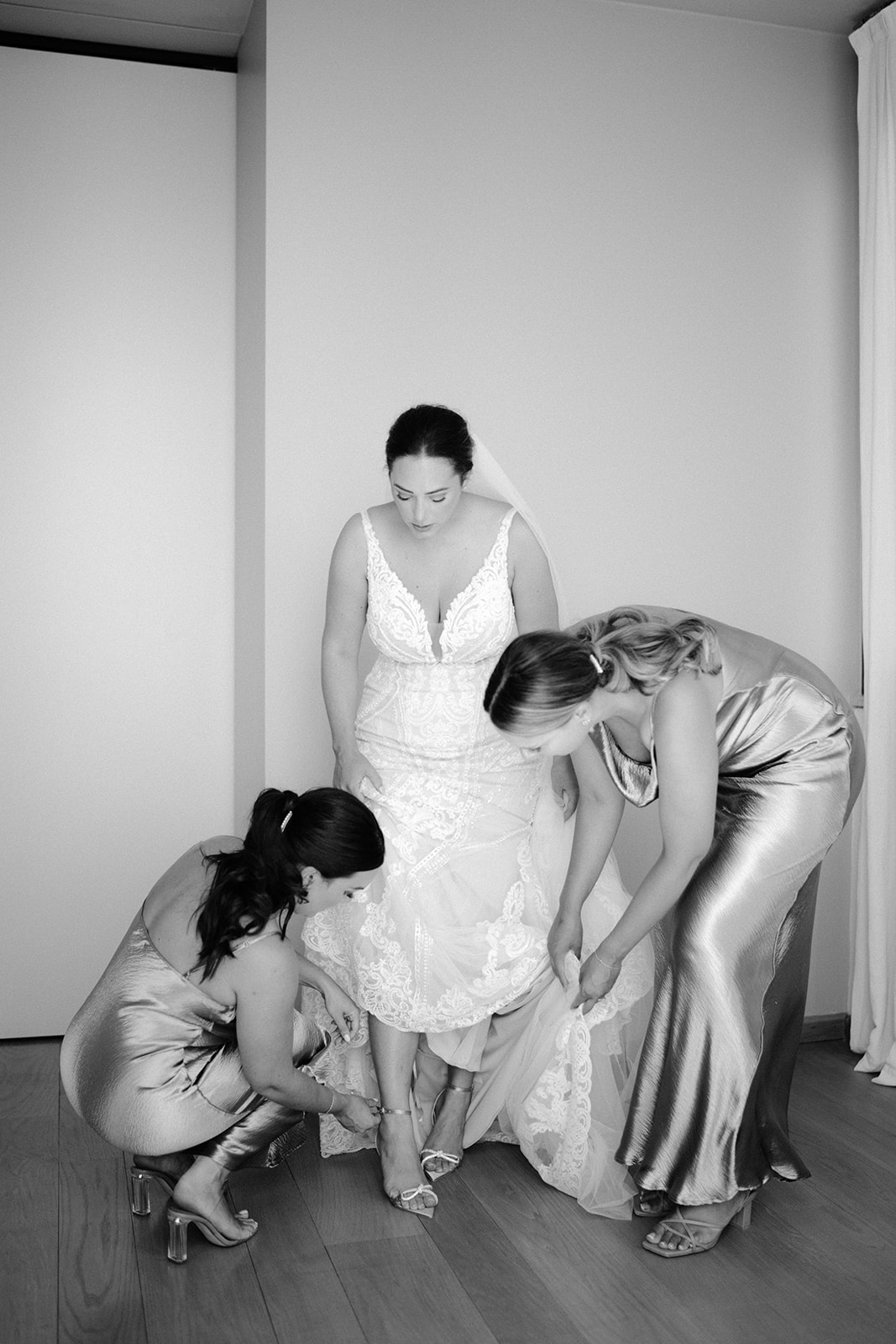 The bridesmaids help the bride fasten her shoes