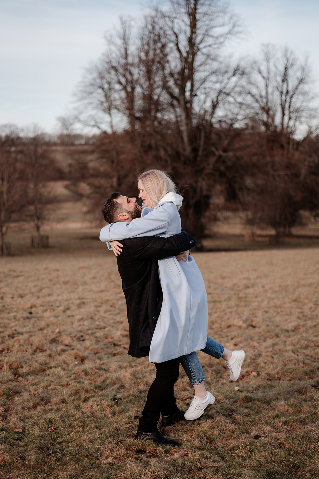 A groom to be lifts his fiance up in a tight embrace on their Hampshire engagement photoshoot