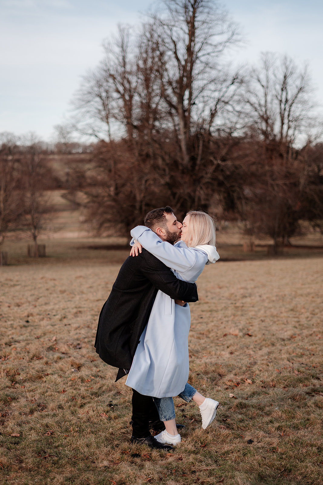 A groom to be lifts his fiance up in a tight embrace and kisses her on their Hampshire engagement photoshoot