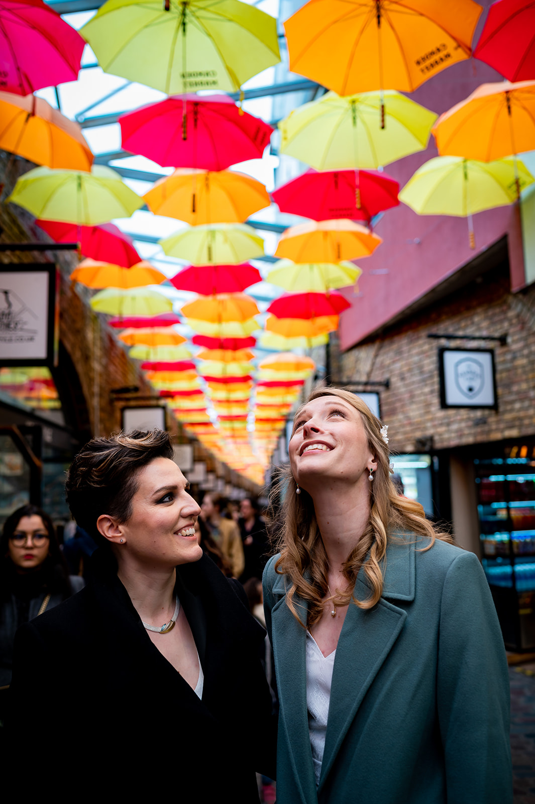 two brides looking up at  brightly coloured umbrellas