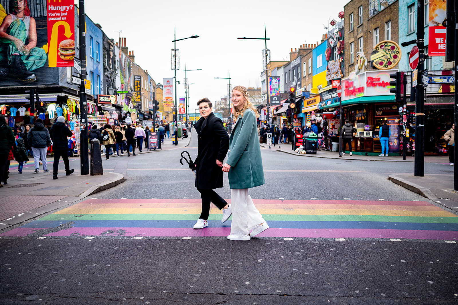 two vibrant brides crossing a Rainbow crossing in Camden