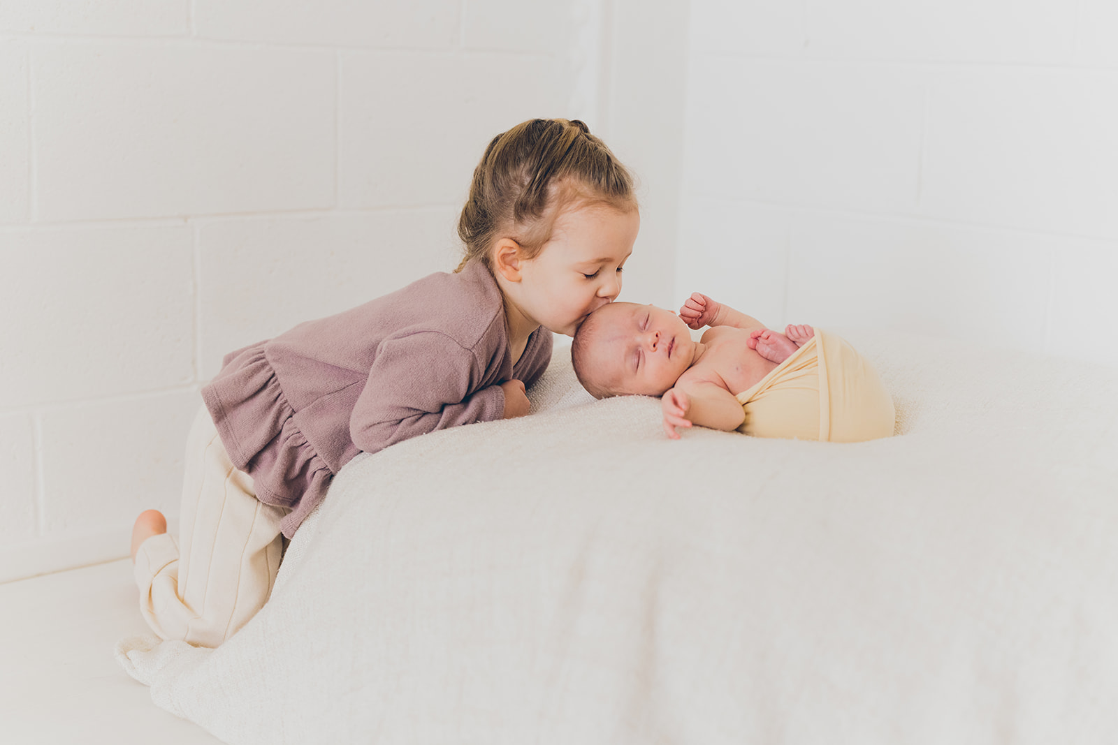 Three year old toddler giving her newborn baby sister a kiss at RinkaDink Studio Northern Ireland.