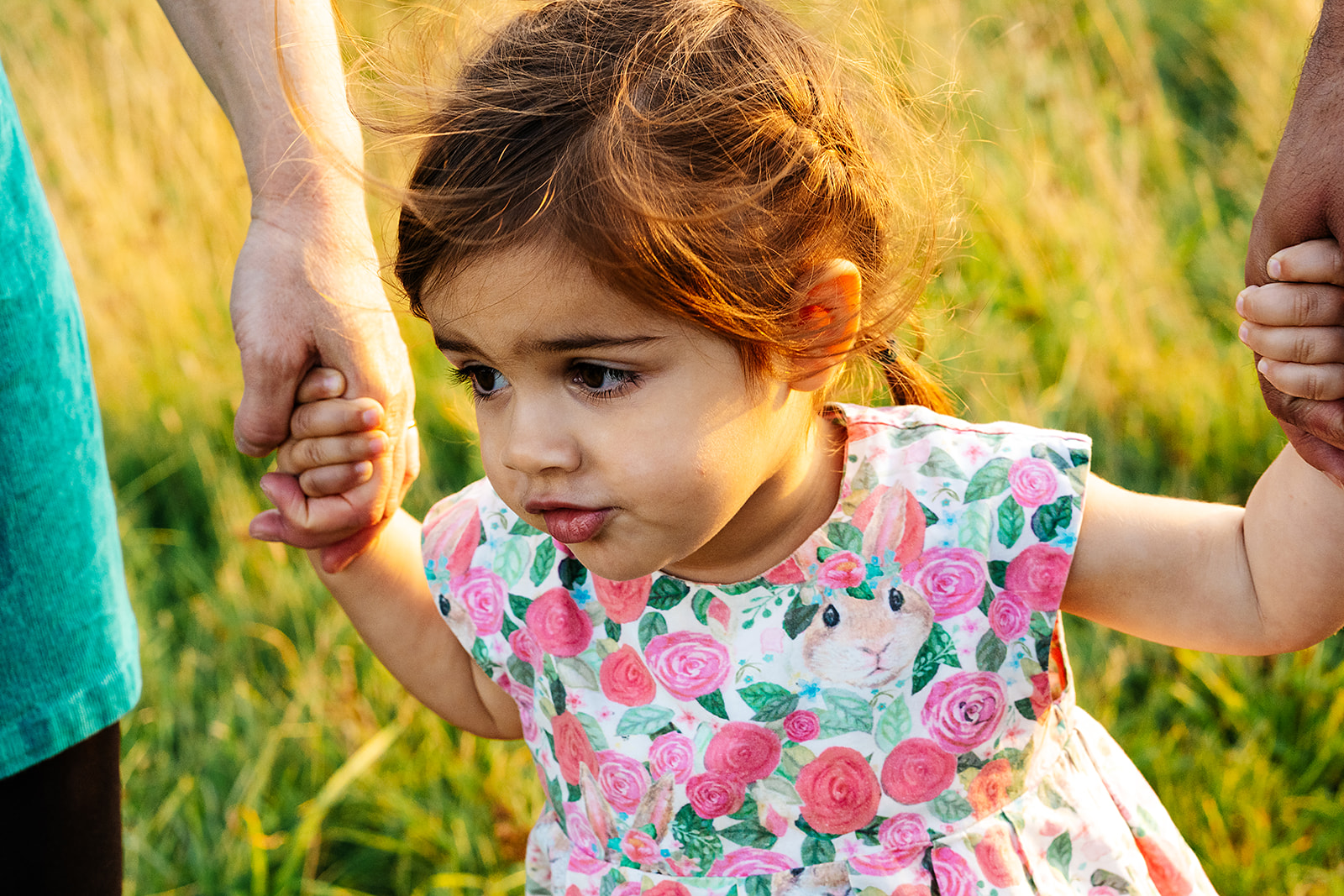 Daughter holding her parents hands as she walks through a field
