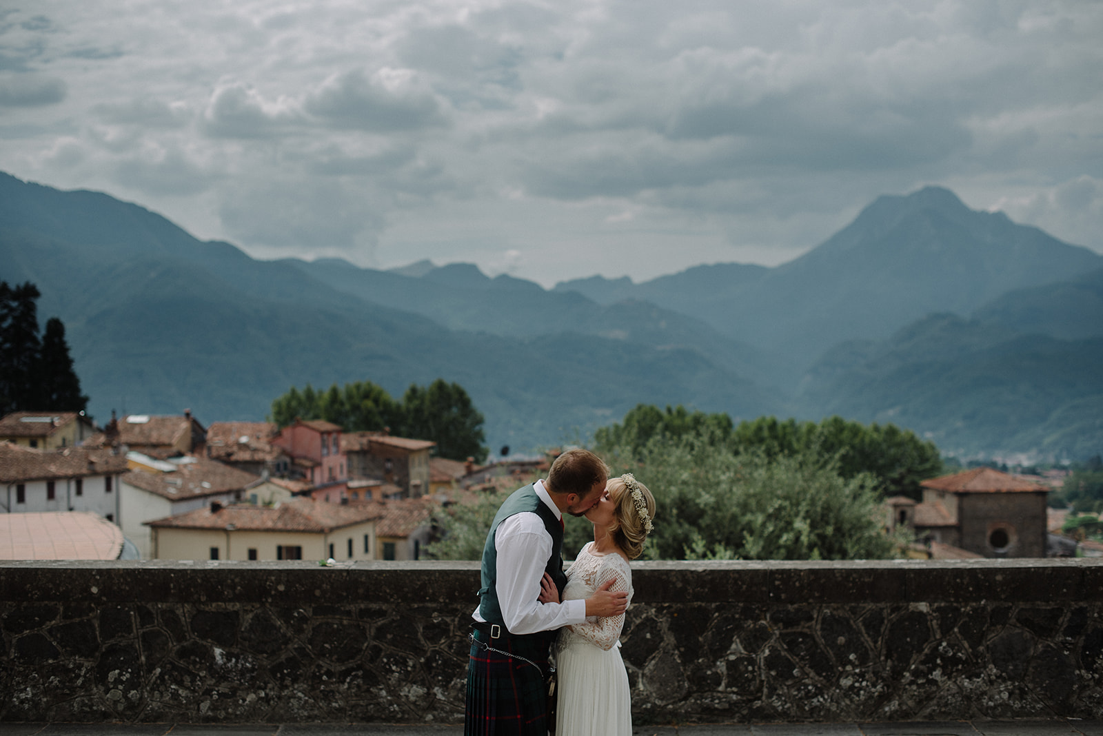 bride and groom share a kiss in Barga with view of mountains and old town on their elopement