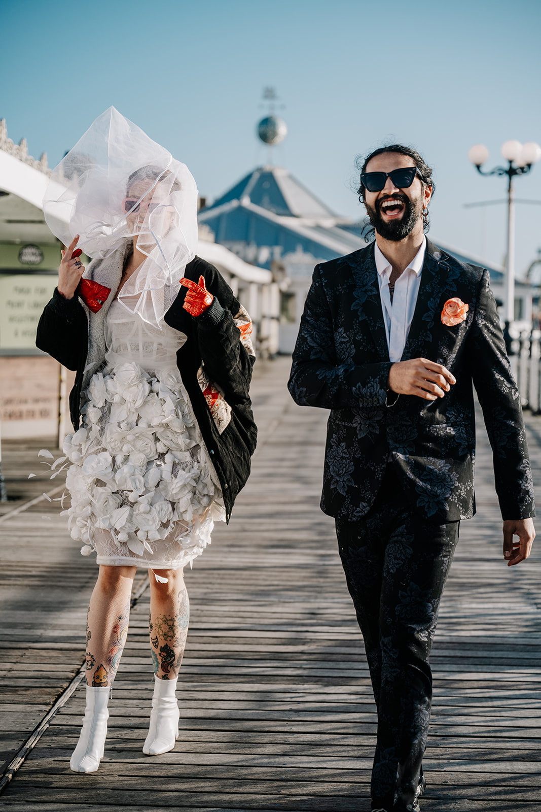 A married couple walking along the pier with the bride's veil blowing in her face