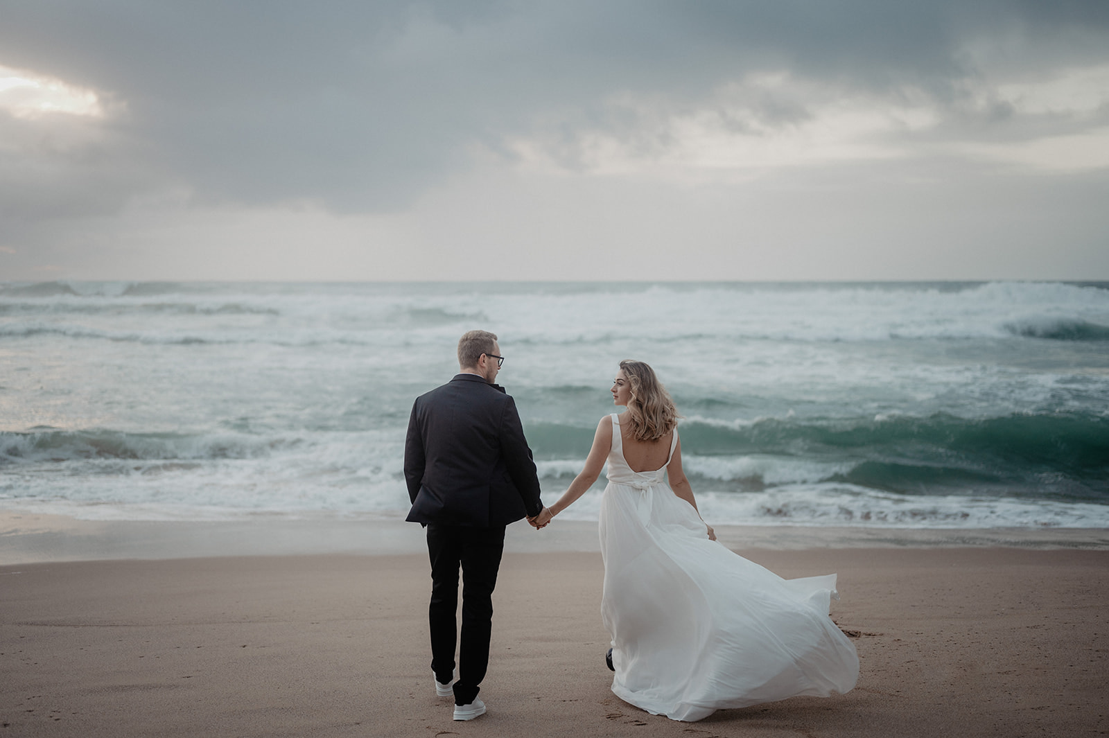 Hochzeitspaar spaziert am Strand von Portugal Richtung Meer