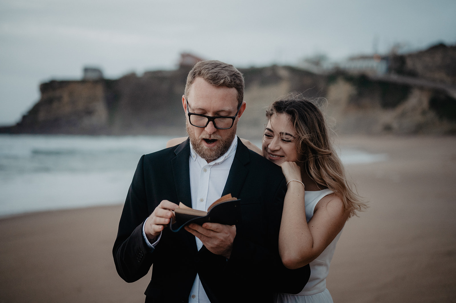 Bräutigam wird von der Braut mit einer freudigen Nachricht überrascht am Strand 