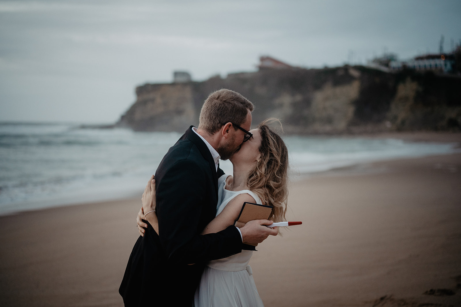 Bräutigam wird von der Braut mit einer freudigen Nachricht überrascht am Strand 