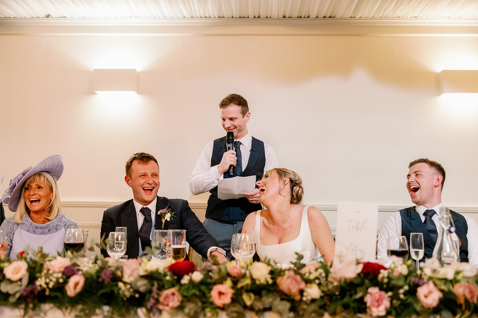 bride and groom laughing as the best man reads his wedding speech