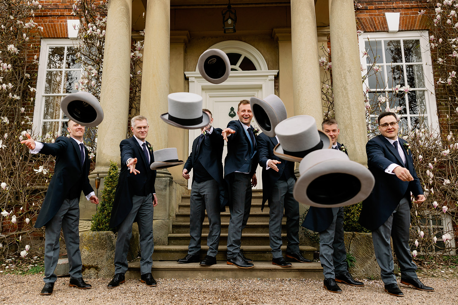 groomsmen throwing their top hats at the camera outside iscoyd park