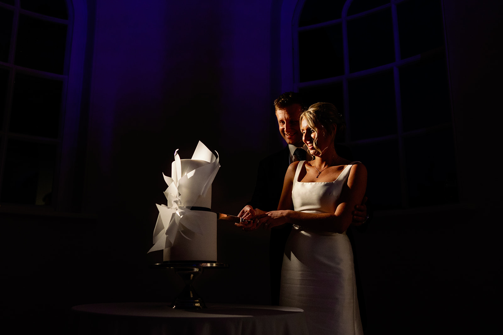 moody photo of the bride and groom cutting their wedding cake at iscoyd park