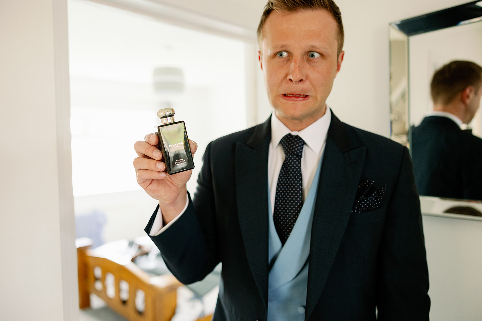 The groom pulling a silly face whilst holding a bottle of Jo Malone fragrance