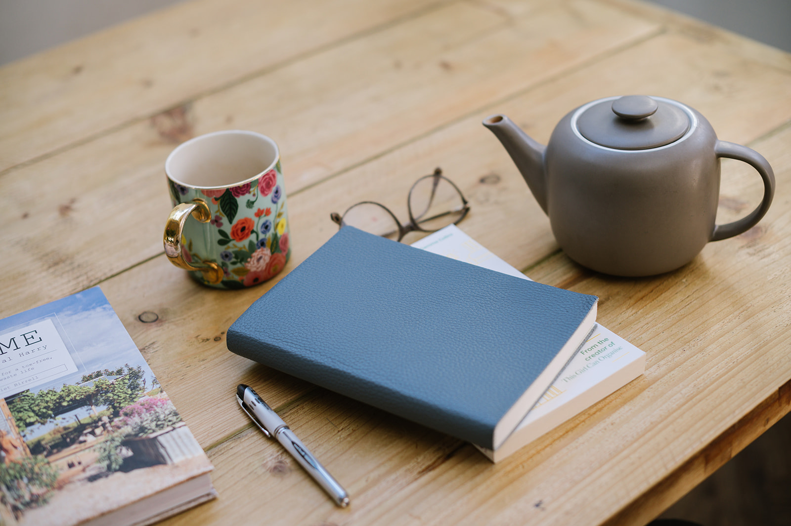 books, tea pot, mug and glasses on a wooden dining table