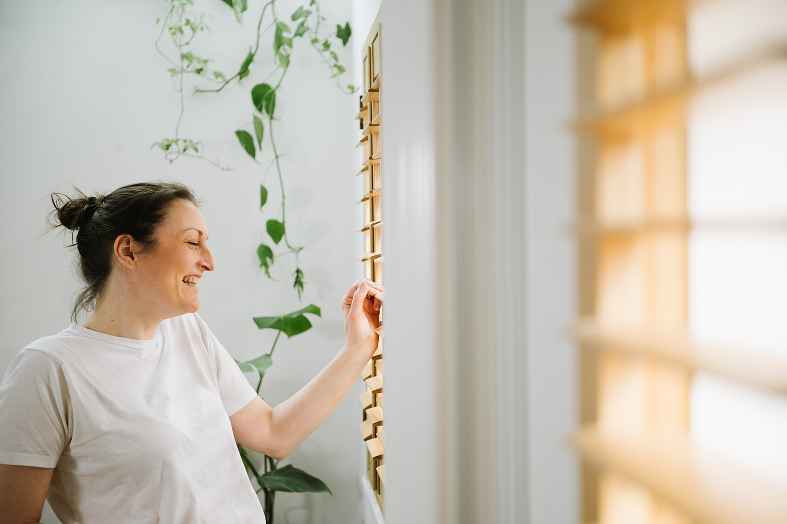 woman looking through window shutters wearing white tshirt