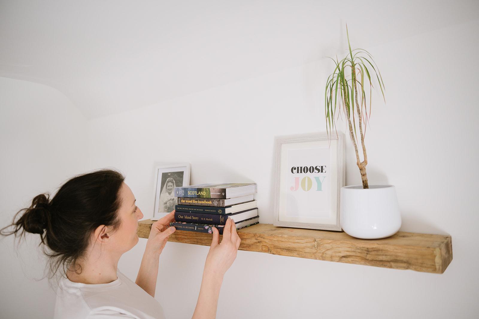 woman in a white t-shirt arranging items on a shelf for her business photos