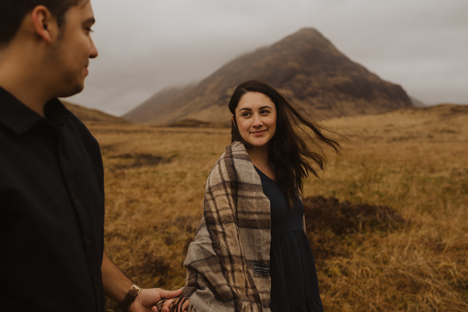 A couple who got engaged in Glencoe walk together with mountain views