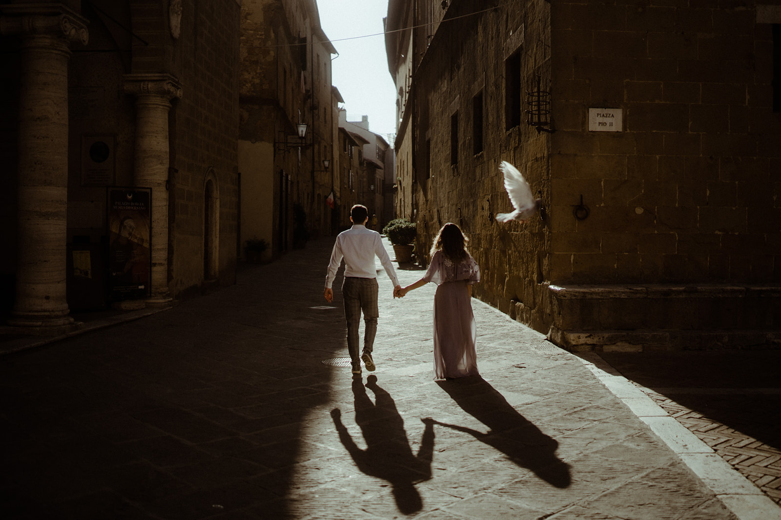 Paar geht in der Stadt Pienza in der Toskana händehaltend durch die Gassen und Taube fliegt vorbei