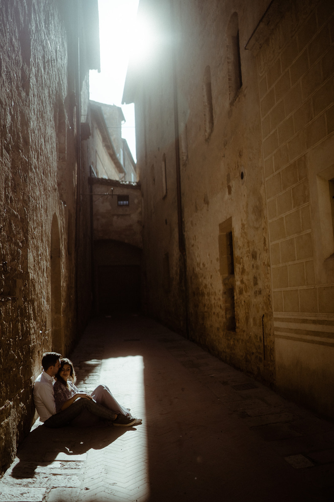 Paar sitzt am Boden in der Stadt Pienza in der Toskana bei einer Fotosession bei Gegenlicht