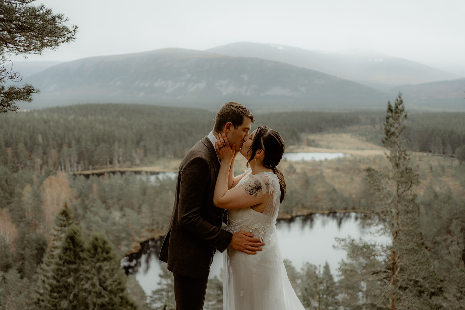 Bride and Groom share a kiss outdoors with view of mountains and lochs