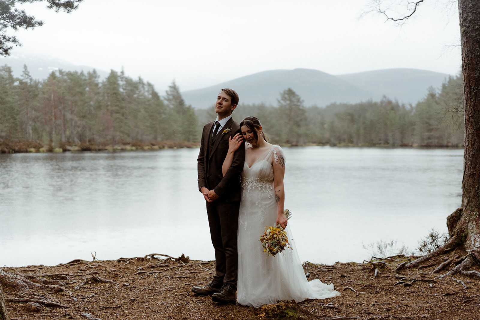 Bride and Groom embrace next to a Scottish Loch with views of the Cairngorm Mountains