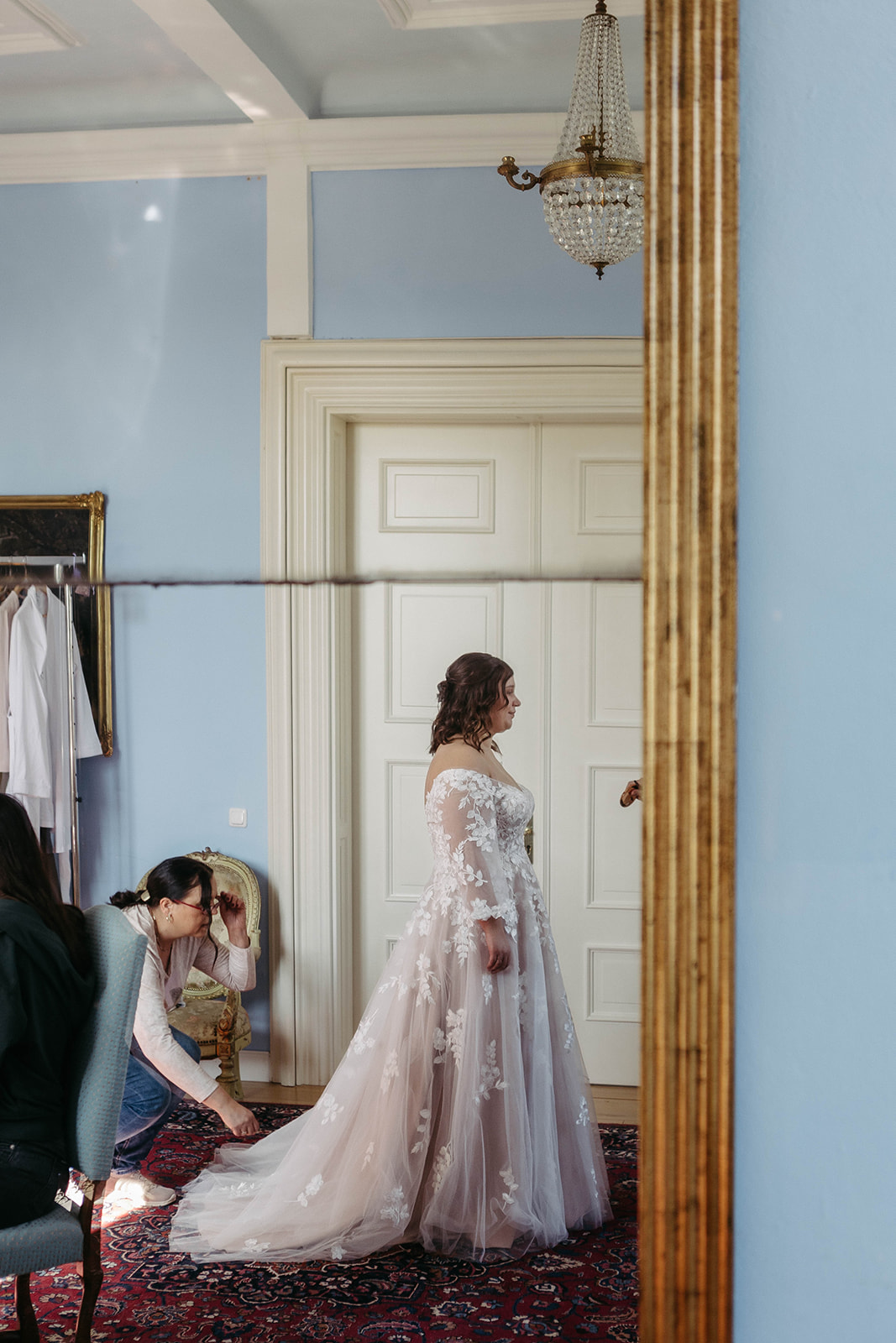 Brautmutter richtet Schleppe im goldumrandeten Spiegel – eleganter Moment der Vorbereitung auf Schloss Jägersburg.