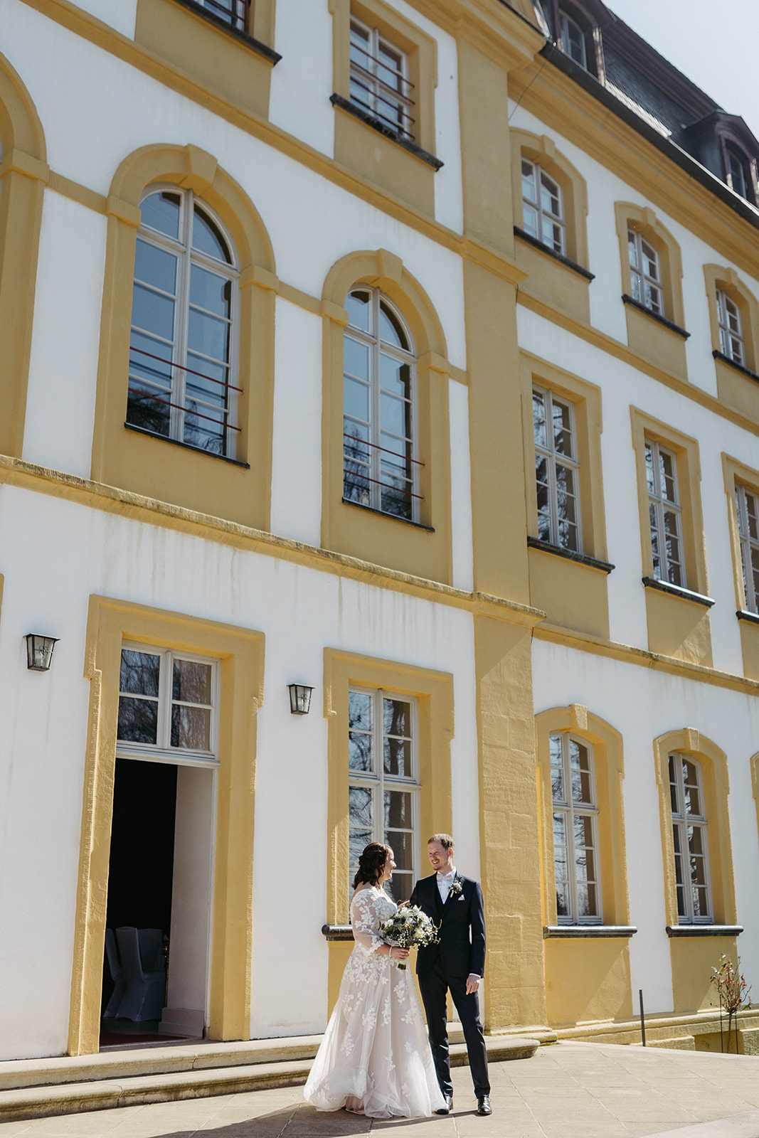 Verträumte Szene: Verliebtes Hochzeitspaar vor imposanter Schlossarchitektur.