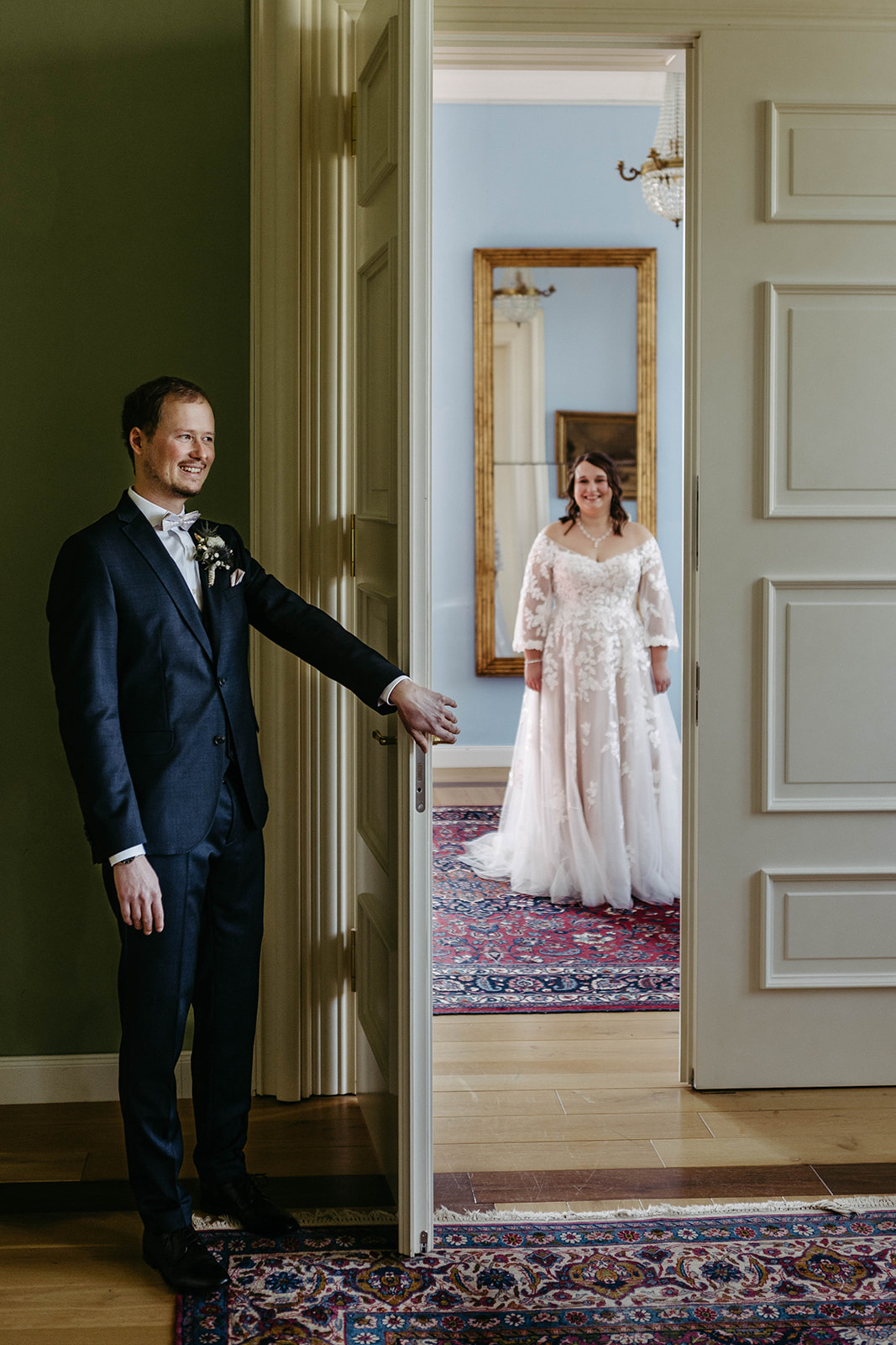 Berührender First Look: Der Bräutigam erwartet die Braut mit dem Rücken zur offenen Tür im Schloss Jägersburg.