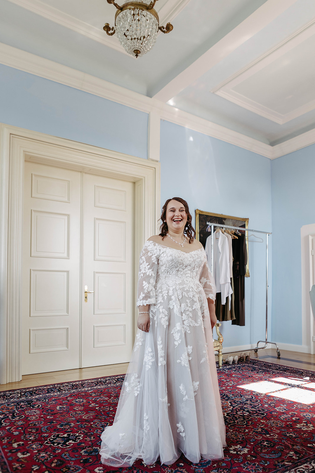 Strahlende Braut in vollem Hochzeitskleid vor Spiegel im historischen Brautzimmer – Eleganz und Vorfreude auf Hochzeit.