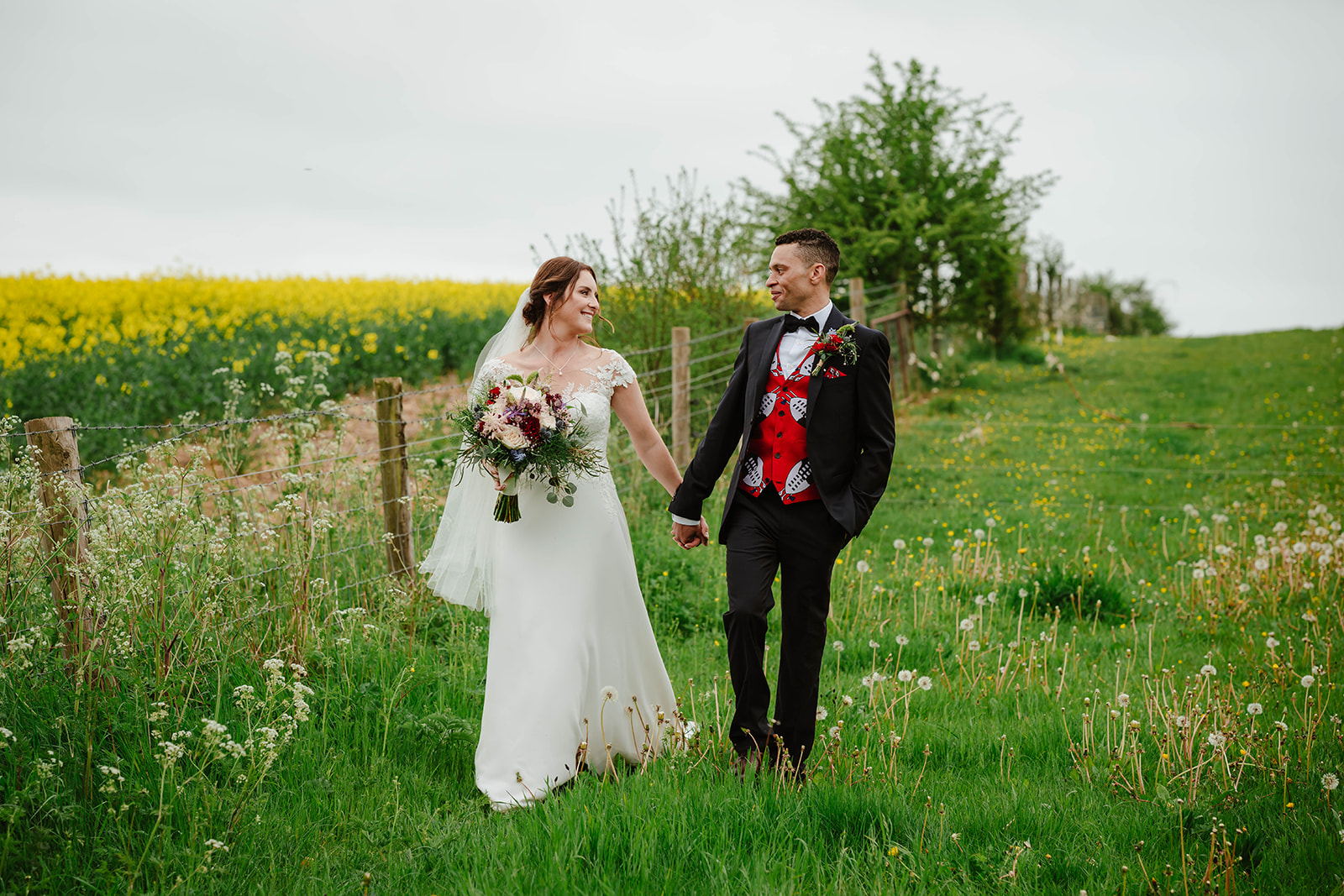 bride and groom walking in field next to rapeseed crop