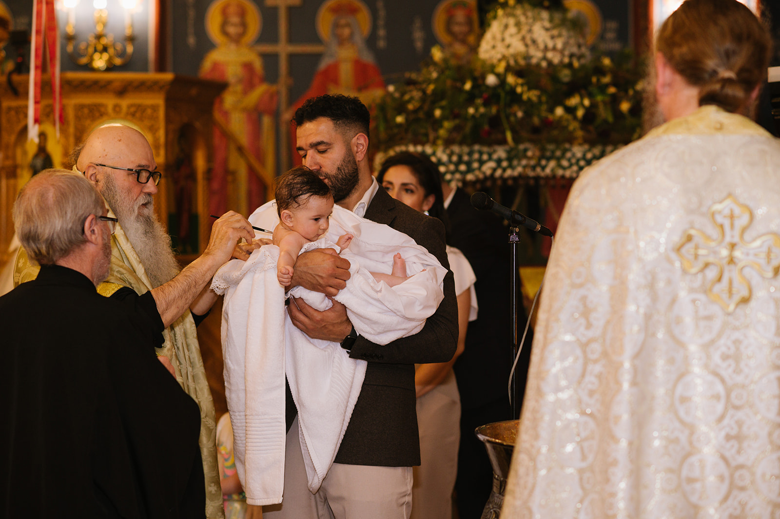 greek orthodox priest anointing the baby with oil at her christening