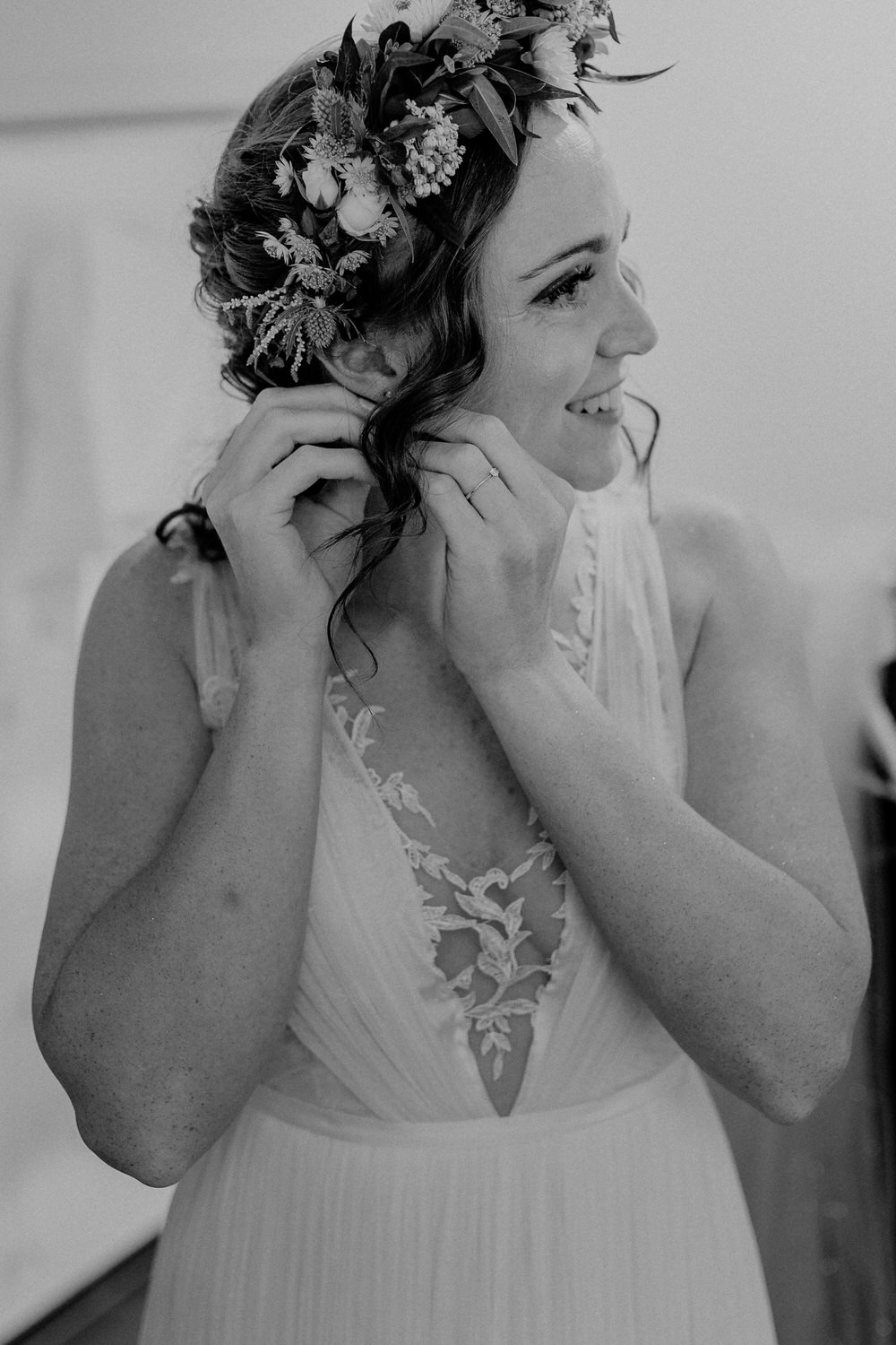 Braut mit Blumenkranz beim Getting Ready steckt ihre Ohrringe an