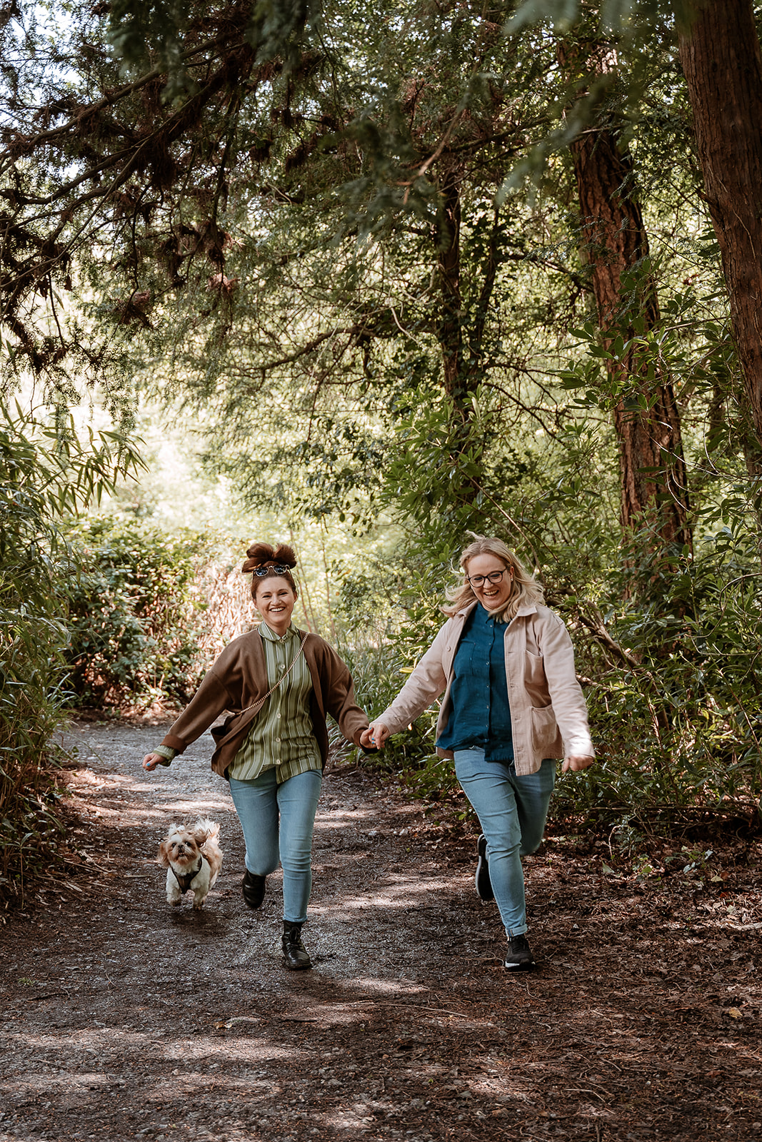 couple run hand in hand together with their dog along a woodland path - couples photography Southampton 