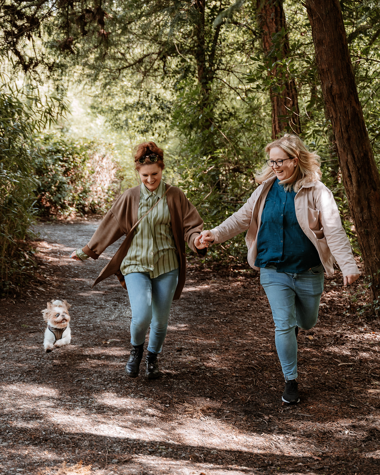 couple run hand in hand together with their dog along a woodland path - couples photography Southampton 
