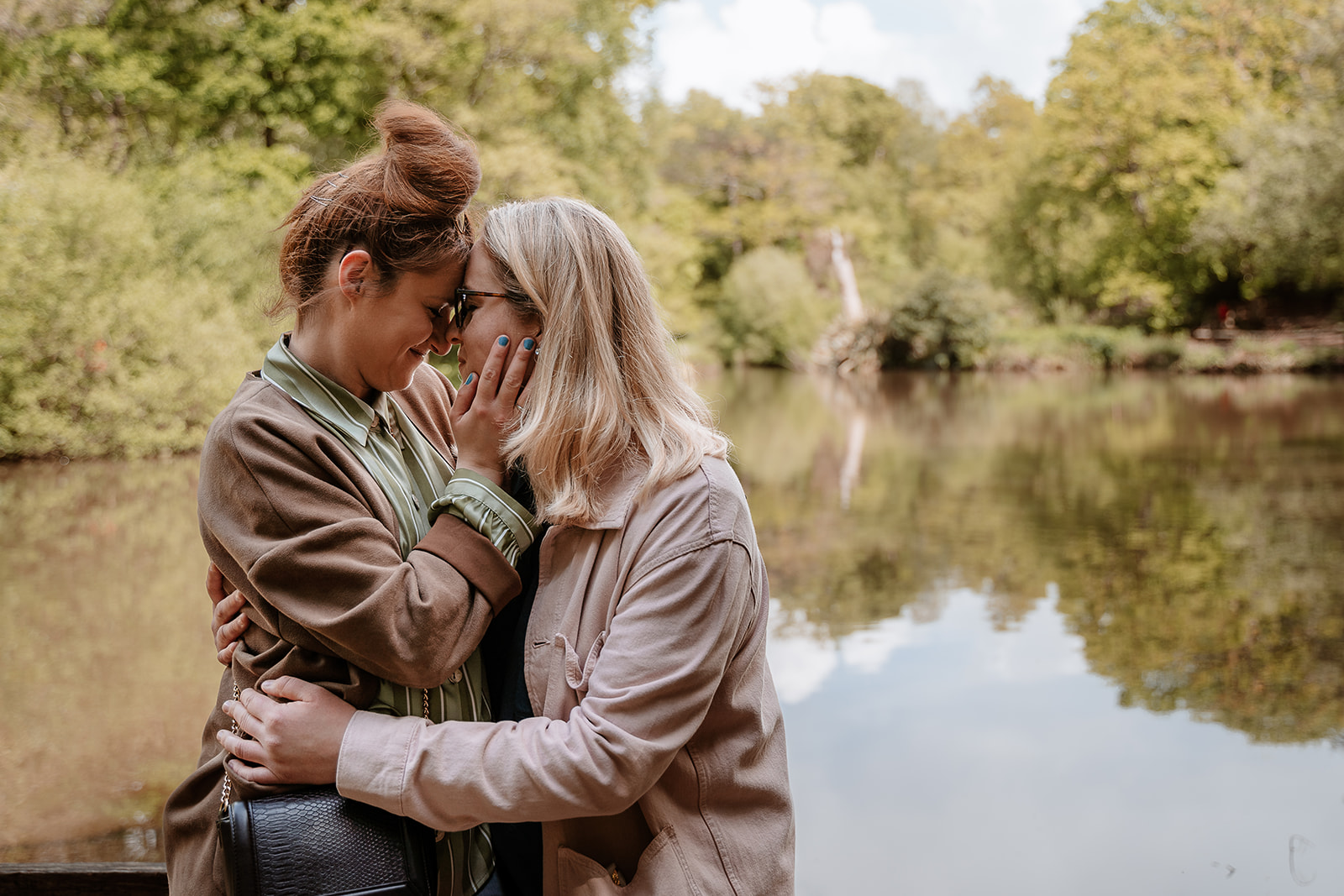 female couple cuddle together with their foreheads touching in front of a lake - Southampton couples photoshoot