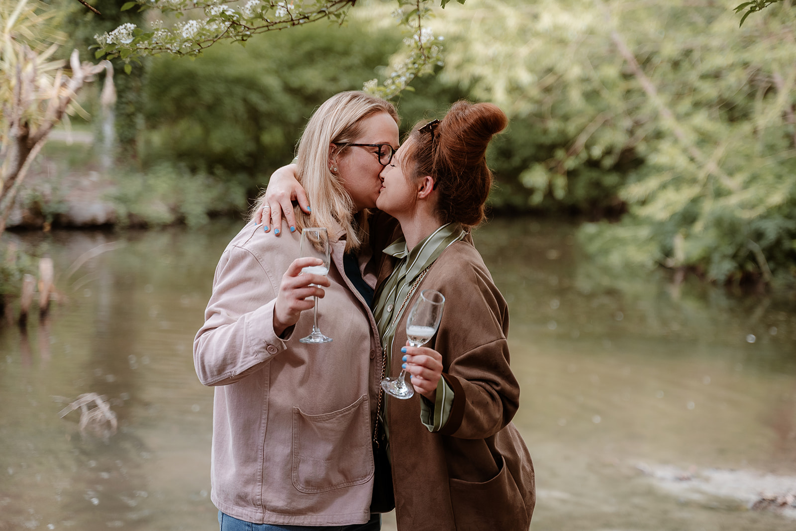 female same-sex couple kiss while holding glasses of prosecco - couples photoshoot in Southampton