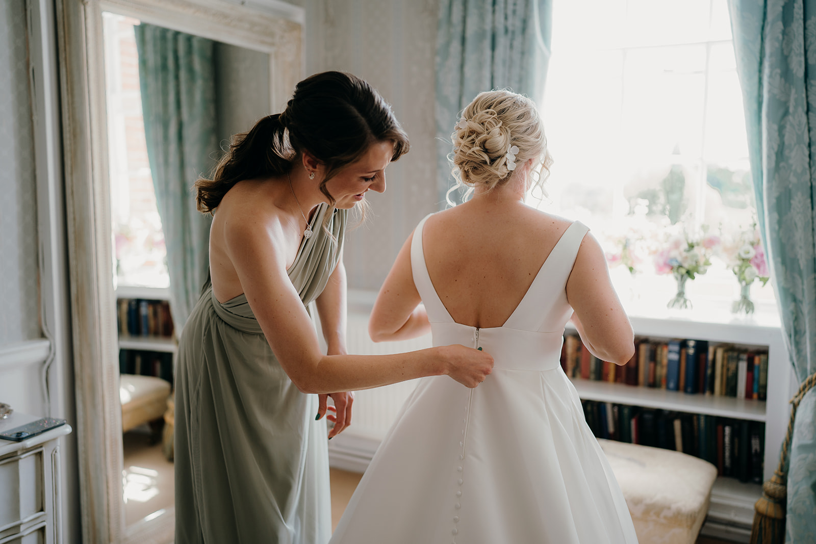 Bride having her dress buttoned by the maid of honour