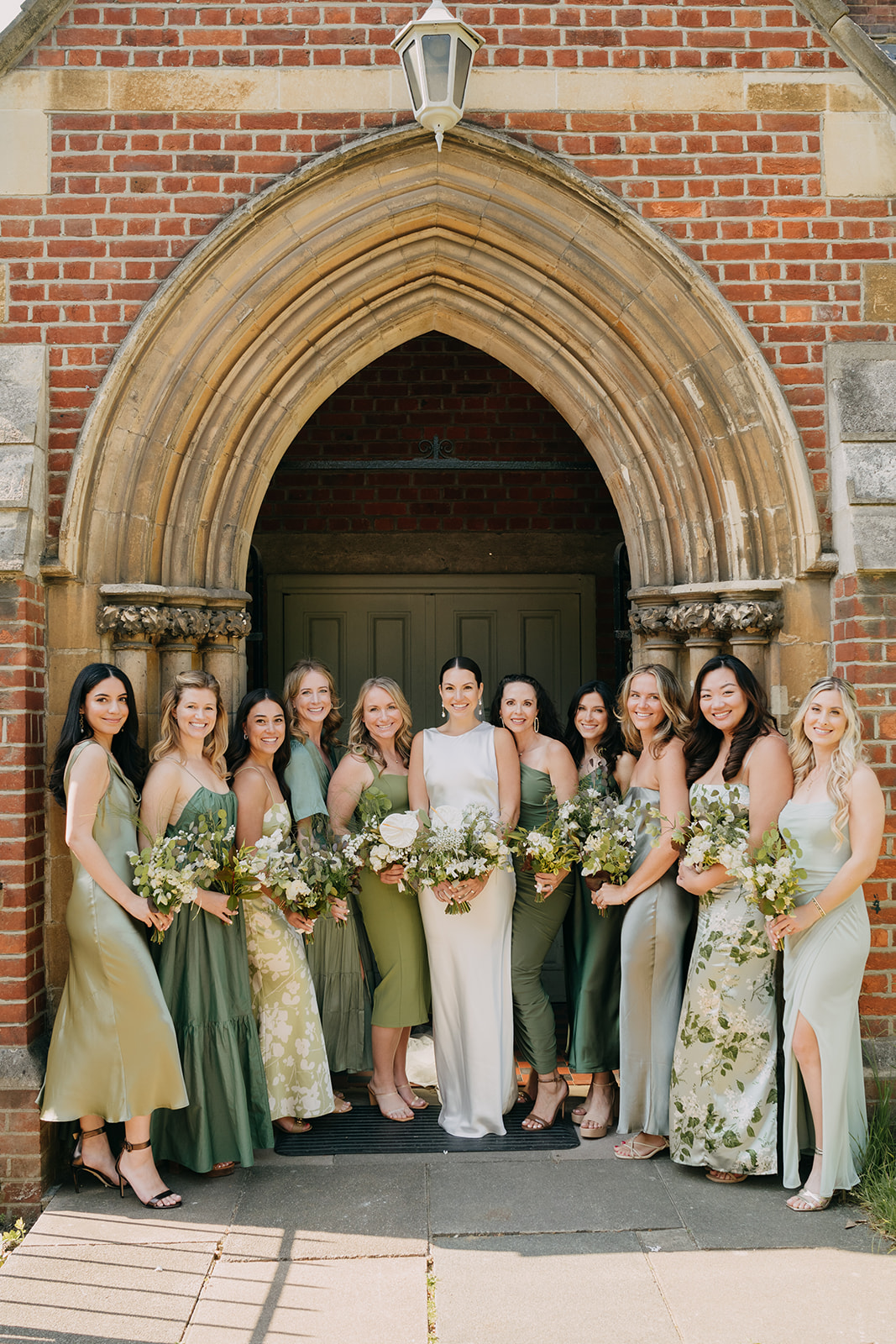 Bride and bridesmaids in mismatched sage green silk dresses and with green and white flowers