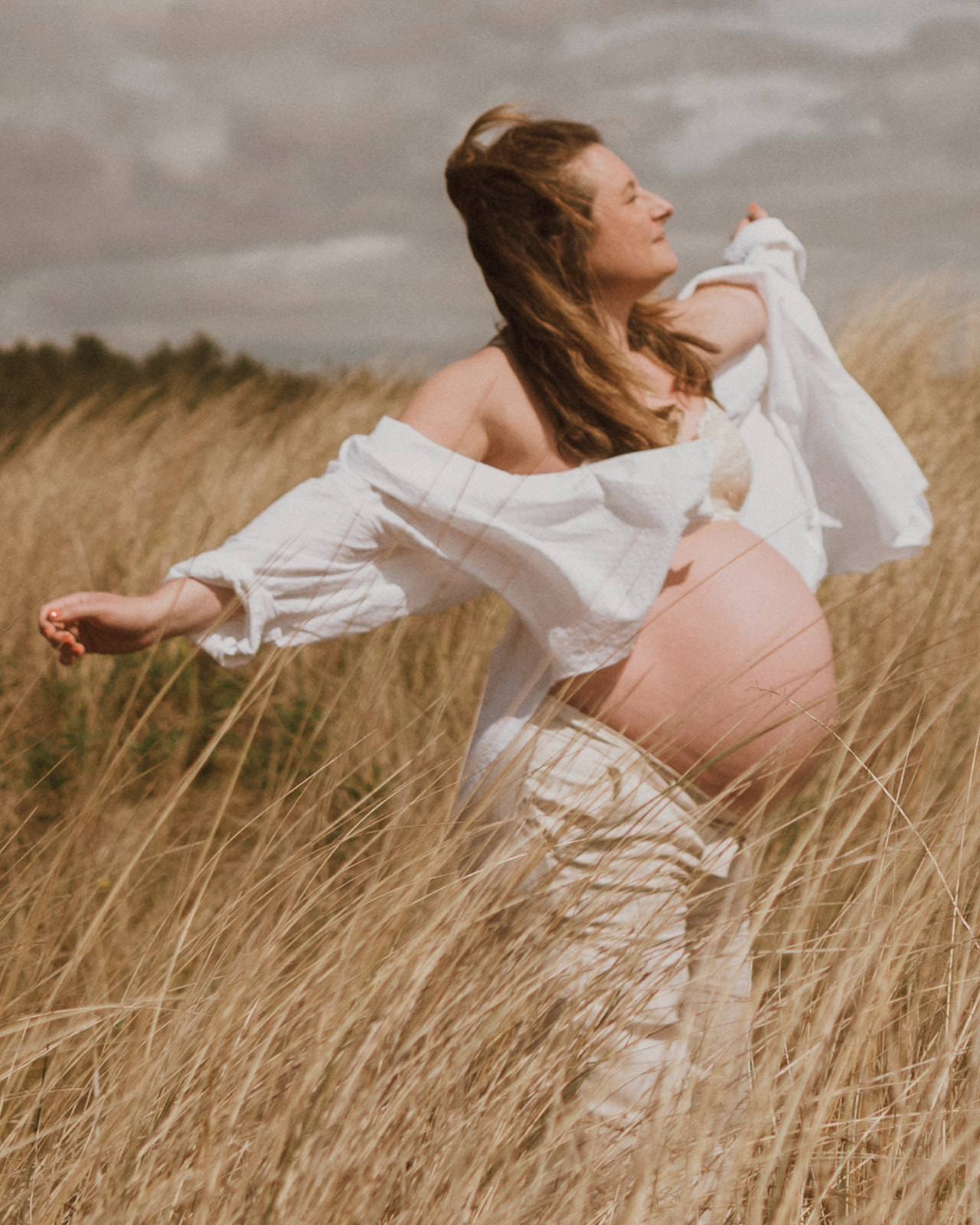 Pregnant lady dances at Tentsmuir Sands during maternity photoshoot with Tamar Hope Photography