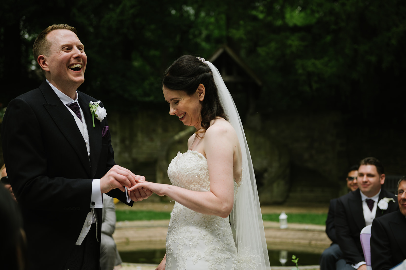 bride and groom laughing as he puts her wedding ring on her finger during the outdoor ceremony