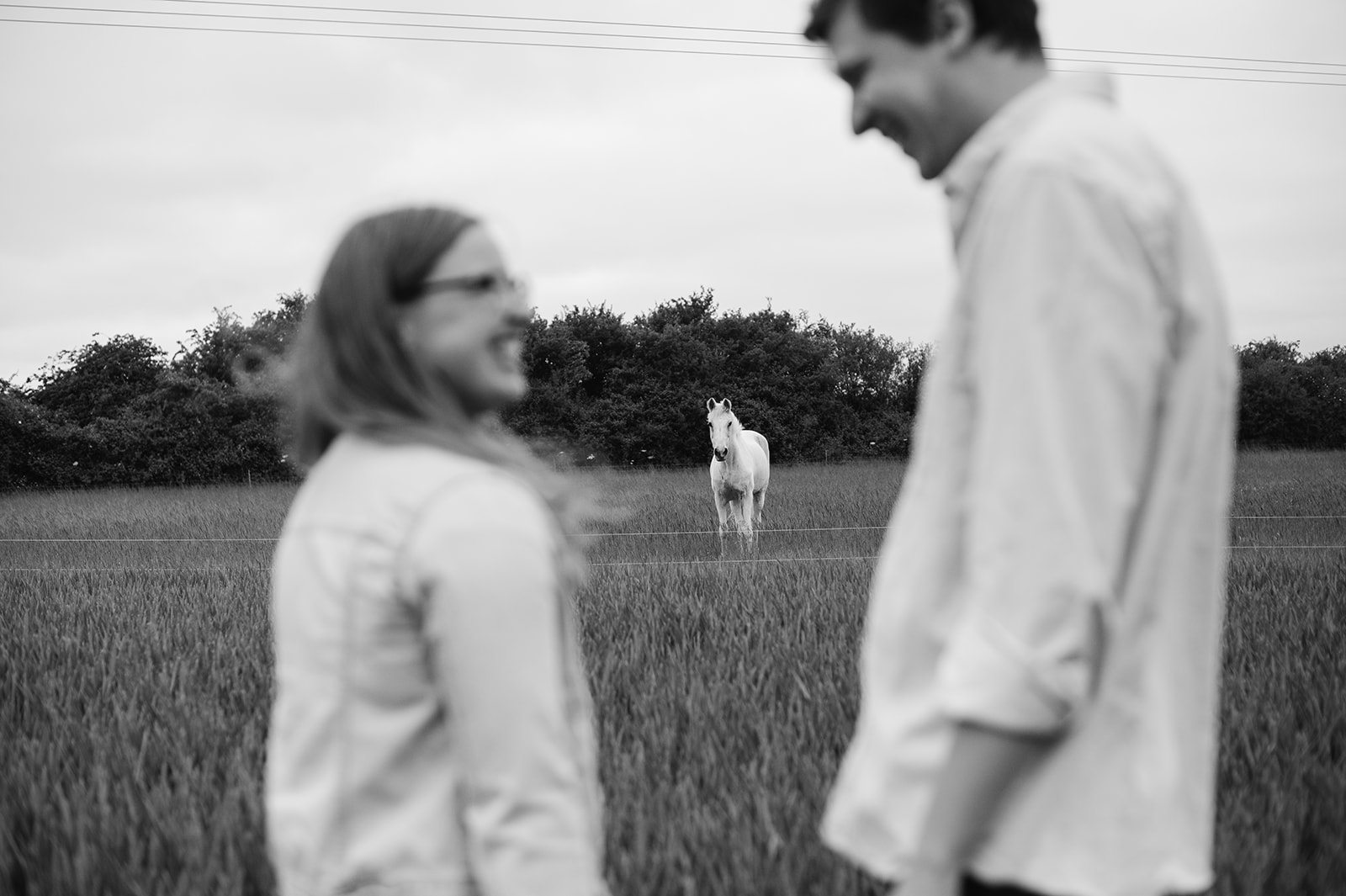 The couple are blurred in the foreground with a white horse framed between them in focus at the middle of the image