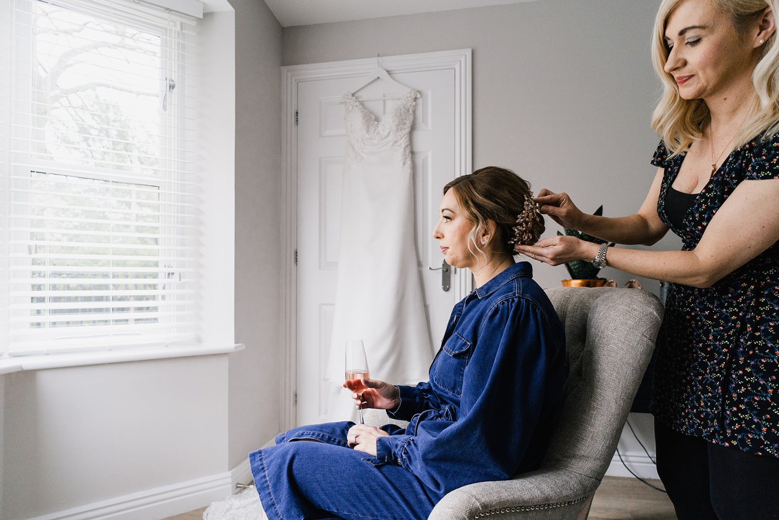 Bride having her hair done in front of wedding dress