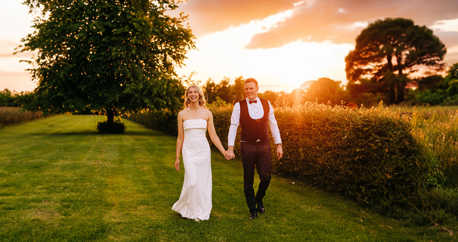 Bride and groom walk hand in hand in castle durrow grounds with sunset behind them