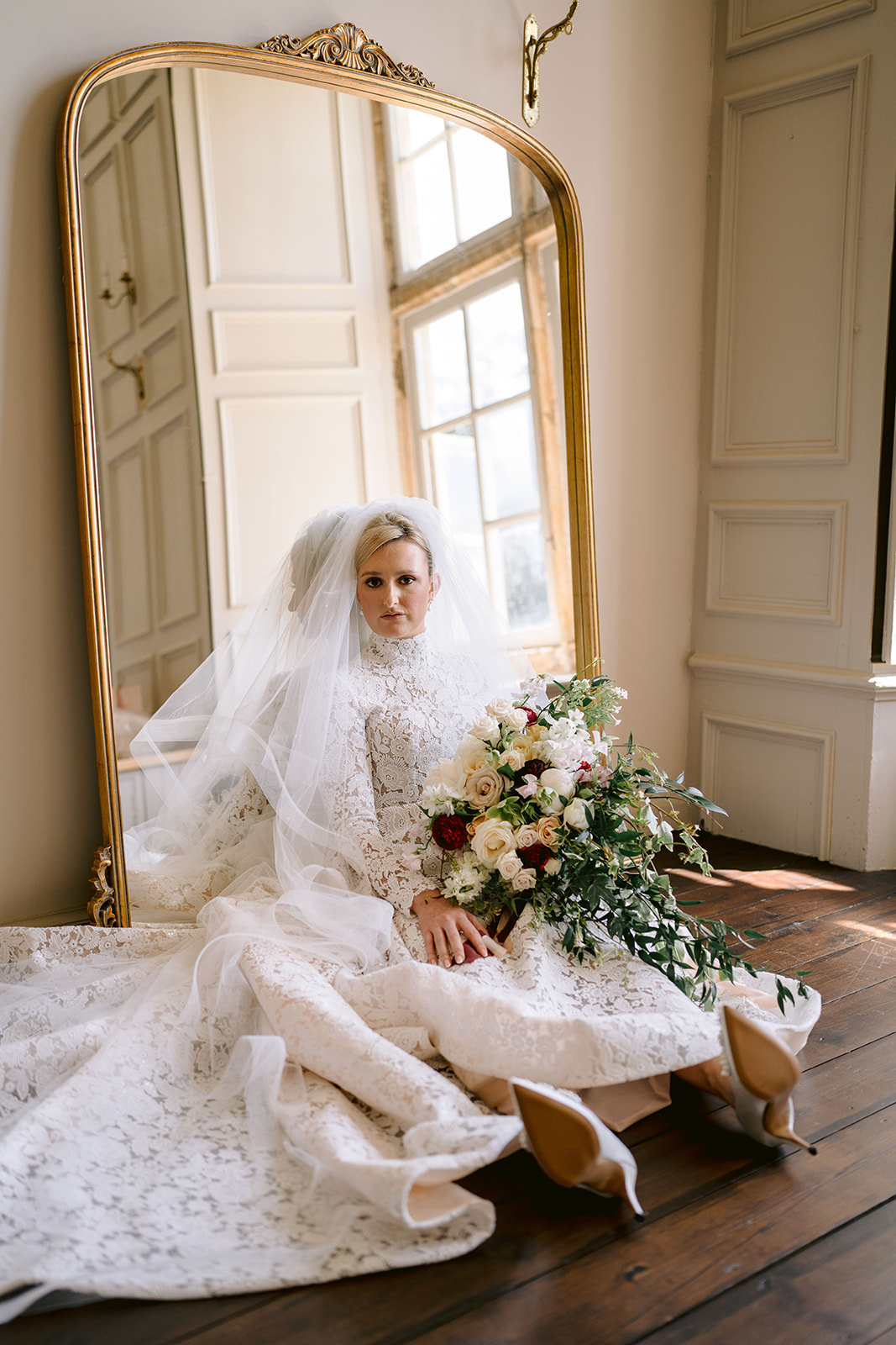 bridal portrait sat on the floor in her wedding dress looking to window with her bouquet