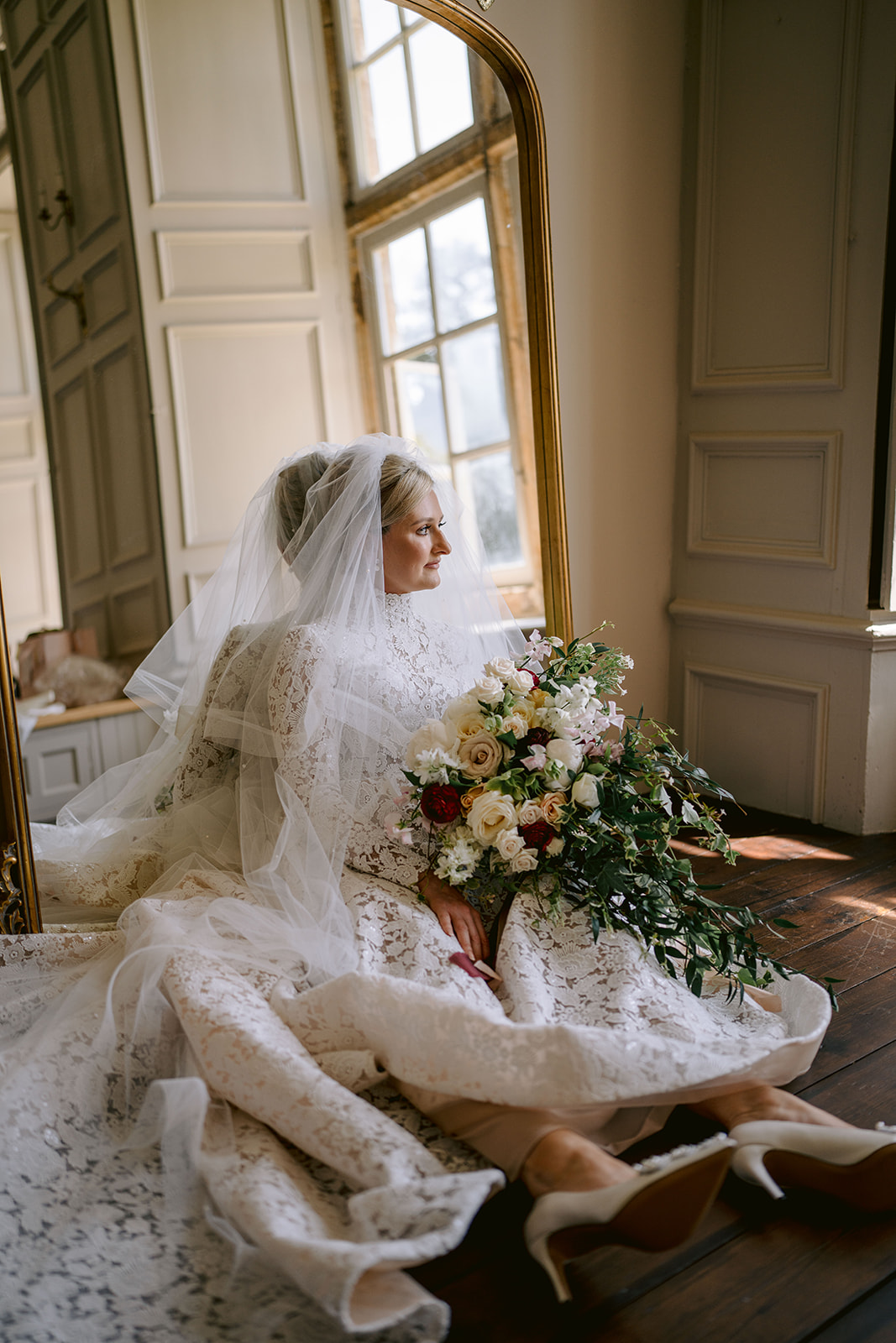 bride portrait sat on the floor in her wedding dress looking to window with her bouquet